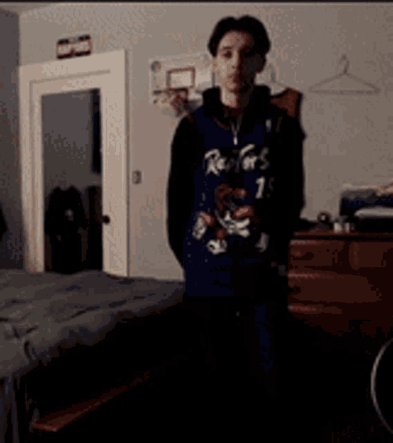a young man wearing a raptors jersey is standing in a bedroom .