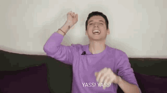a young man in a purple shirt is sitting on a couch and making a funny face .