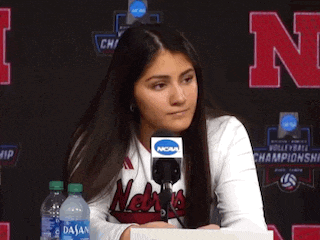 a woman wearing a nebraska shirt is sitting at a desk with a microphone