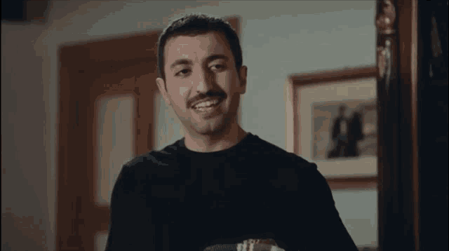 a man with a mustache is smiling in a room