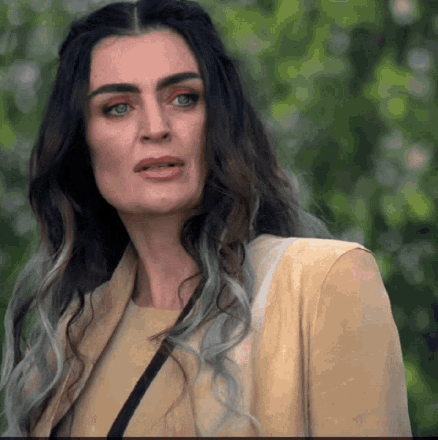 a woman with long black hair and gray streaks is wearing a yellow jacket