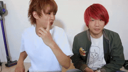 two young men with red hair are sitting next to each other and one of them is pointing at the other .