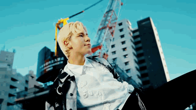a man with blonde hair is sitting in front of a building with a crane in the background .