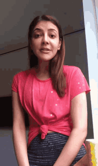 a woman in a pink shirt and blue shorts is standing in front of a window and making a funny face .