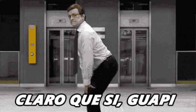 a man in a suit and tie is standing in front of an elevator with the words claro que si guapi written above him .