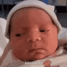 a baby is wearing a white hat and making a sad face .