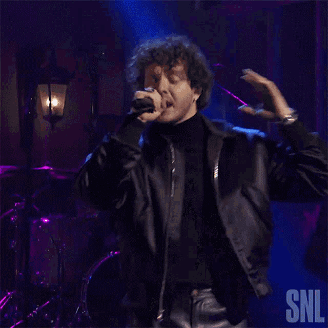 a man in a black jacket is on stage with a snl logo in the corner