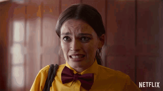 a woman wearing a yellow shirt and a burgundy bow tie with a netflix logo in the background