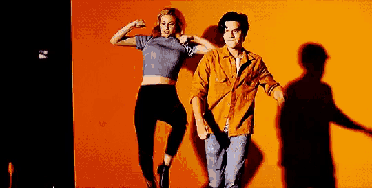 a man and a woman are dancing in front of an orange wall while holding hands .