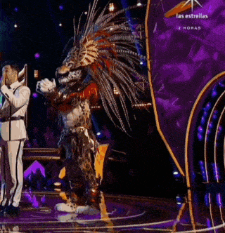 a man in a native american costume stands on a stage with a las estrellas sign behind him
