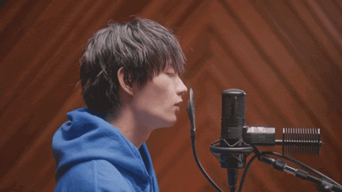 a young man in a blue hoodie sings into a microphone