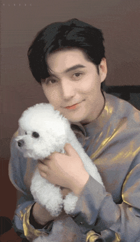 a man in a gold shirt is holding a small white poodle