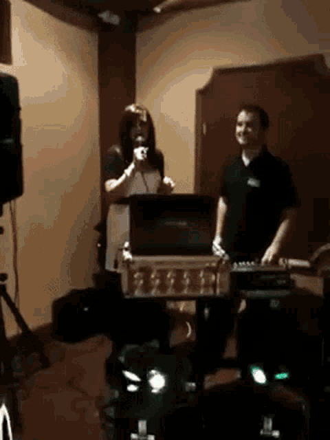 a woman singing into a microphone while a man stands behind her
