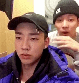 a man wearing a black hat and a blue jacket is sitting next to another man wearing a beanie .