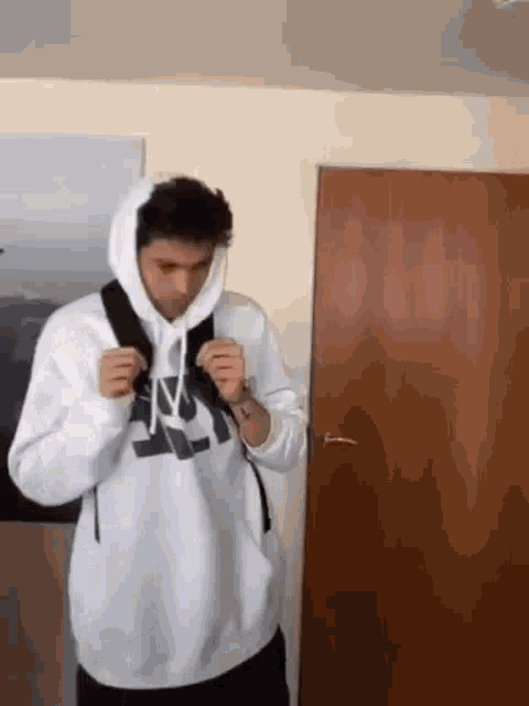 a man wearing a white hoodie and a backpack is standing in a room .