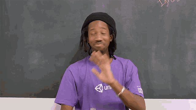 a man wearing a purple unity shirt waves his hand in front of a blackboard