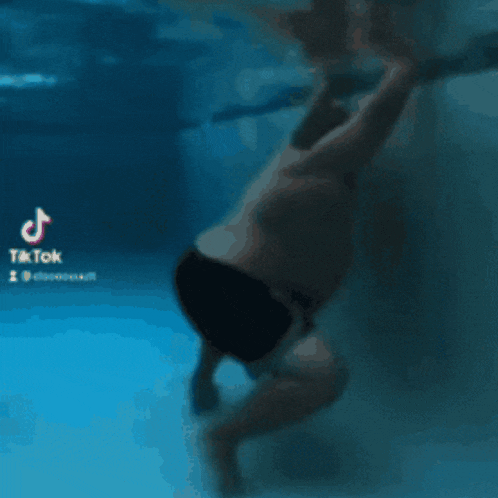 a man without a shirt is swimming underwater in a pool with a tiktok logo in the corner