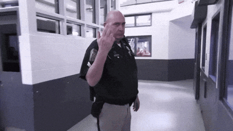 a police officer giving the middle finger while walking down a hallway