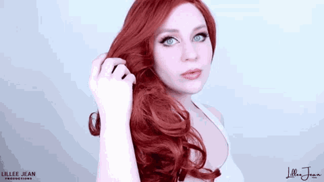 a woman with long red hair and blue eyes is holding her hair in her hand .