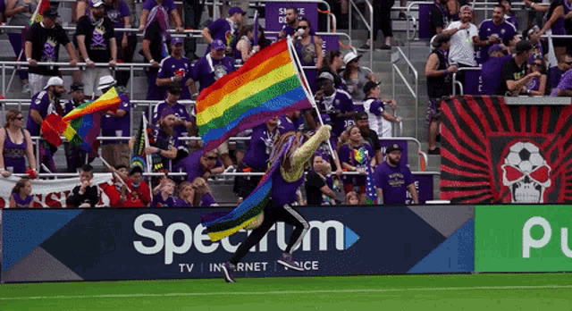 a man holding a rainbow flag stands in front of a spectrum sign