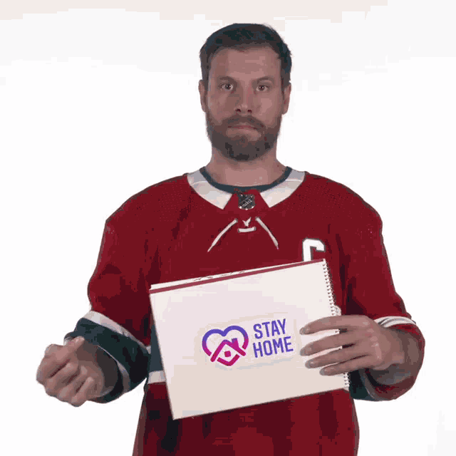 a man in a red jersey is holding a paper that says stay home