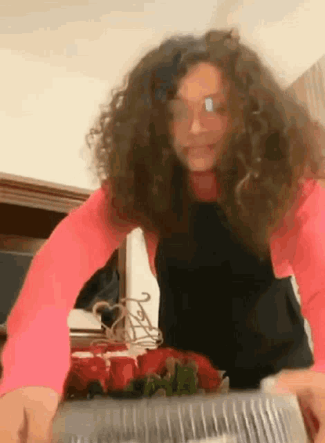 a woman with curly hair wearing glasses and a pink shirt