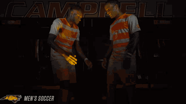 two men giving each other a high five in front of a banner that says campbell men 's soccer