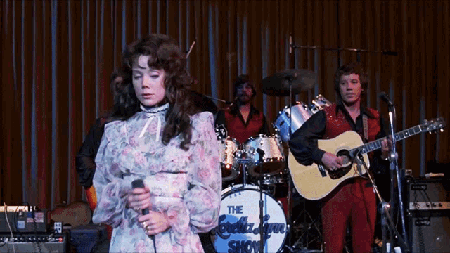 a woman is singing in front of a drum set that says the beetlejuice show