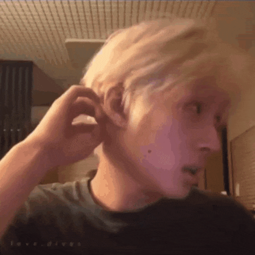 a man with blonde hair is adjusting his ear with his hands .