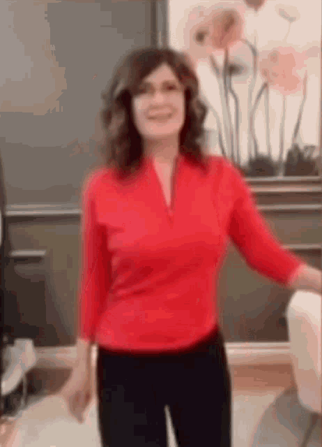 a woman in a red shirt and black pants is standing in front of a painting of flowers .