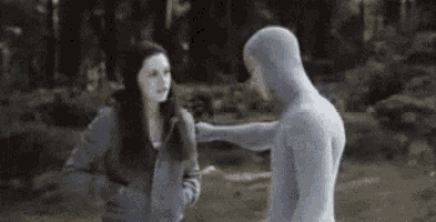 a man and a woman are standing next to each other in the woods . the man is wearing a hoodie .