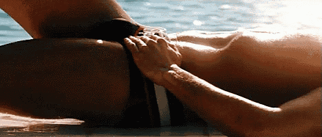 a man in a bathing suit is laying in the water with his hand on his thigh .
