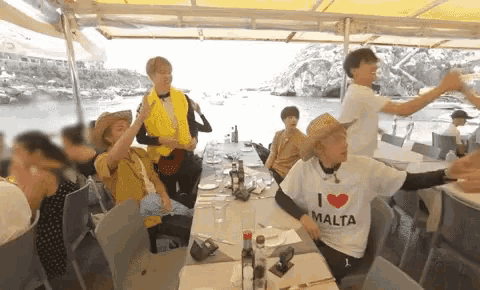 a group of people are sitting at a table with one wearing a shirt that says i love malta .