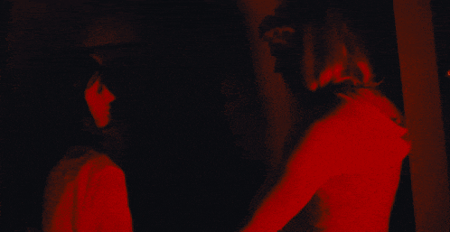 a woman in a red shirt stands next to another woman in a red light