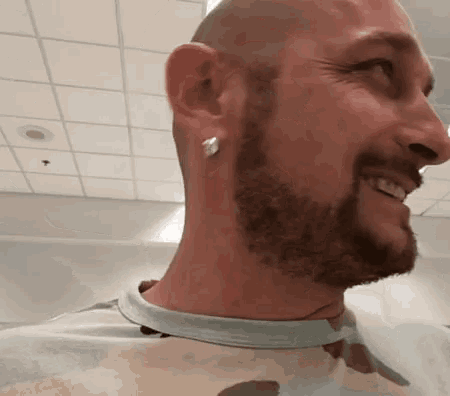 a man with a beard and earrings on his ears is smiling and looking at the camera .