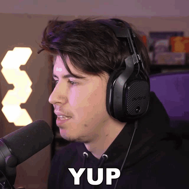 a man wearing headphones is talking into a microphone and the word yup is above him