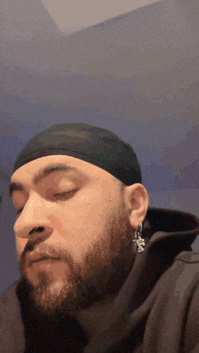 a man with a beard wearing a black headband and earrings with the letter m on them
