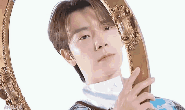 a young man is holding a mirror in his hand and looking at himself .