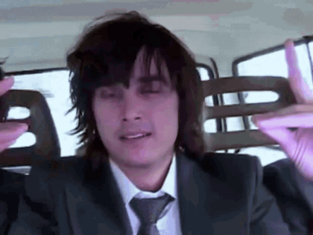 a man in a suit and tie is sitting in a car with his eyes closed