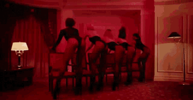 a group of women in lingerie are dancing in a room with red lights .