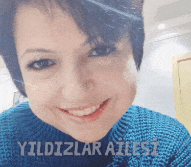 a woman in a blue sweater is smiling with the words " yildizlar ailesi " behind her