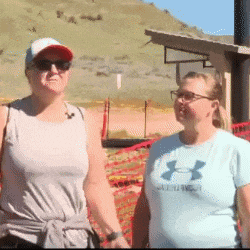 two women are standing next to each other and one is wearing an under armour shirt .