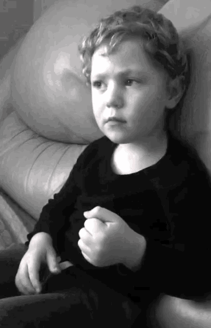 a young boy with curly hair is sitting on a white couch