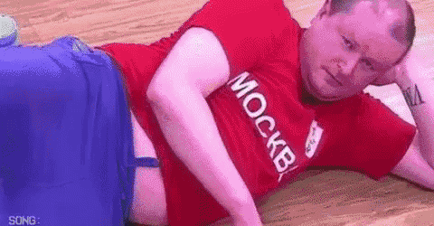 a man in a red shirt is laying on the floor with his head on his hand .