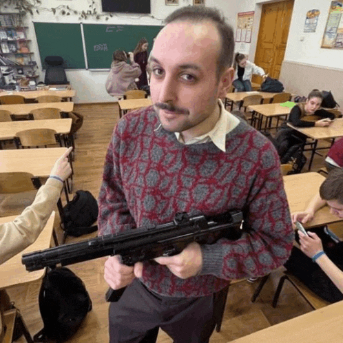 a man in a sweater holds a gun in a classroom with a chalkboard that says ' russia '