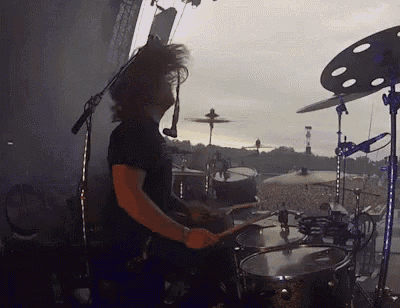 a man in a black shirt is playing drums in front of a crowd .