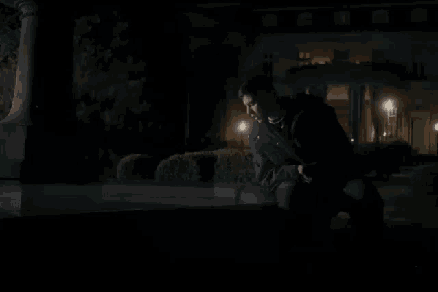 a man in a black jacket is kneeling down in front of a house at night .