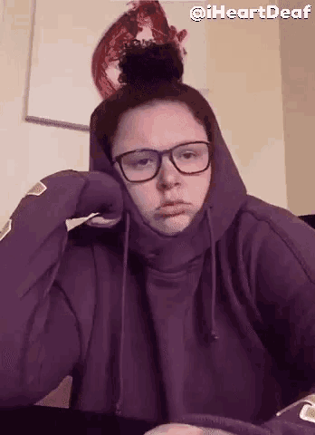 a woman wearing glasses and a purple hoodie is sitting at a table .