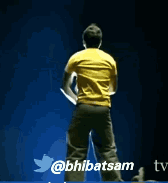 a man in a yellow shirt stands with his arms outstretched in front of a twitter icon