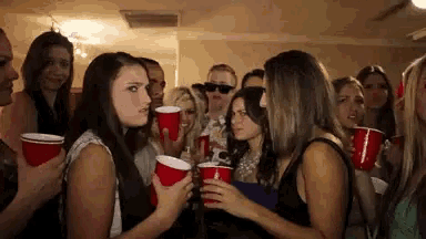 a group of young women are holding red cups and talking to each other at a party .